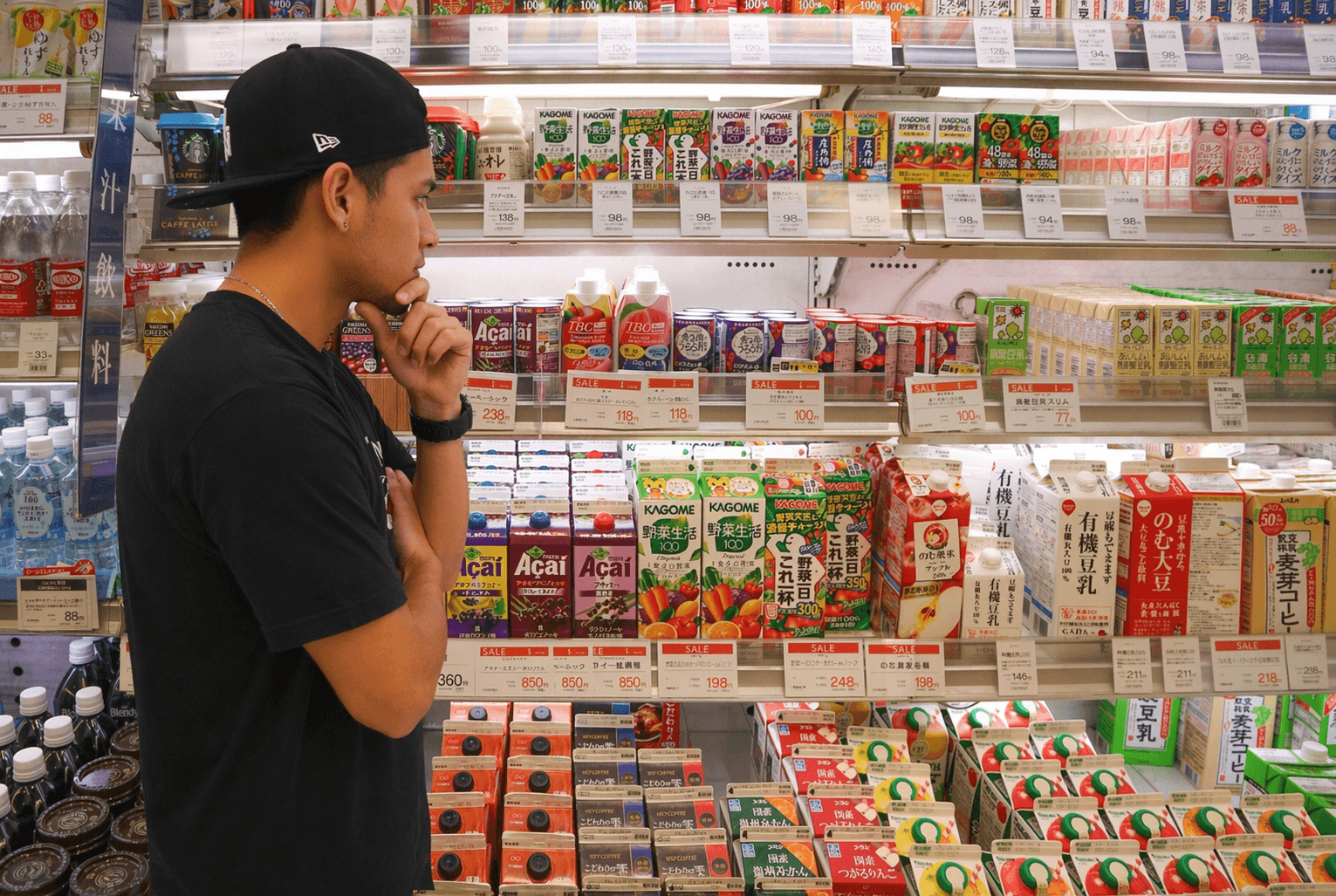 Homem analisa preços de bebidas em prateleira de supermercado no Japão, refletindo impacto do aumento do custo de vida